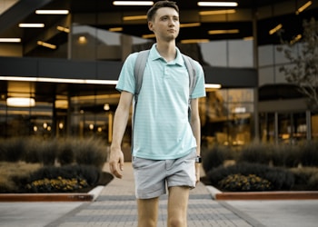 man in green crew neck t-shirt and blue denim shorts standing on gray concrete pavement