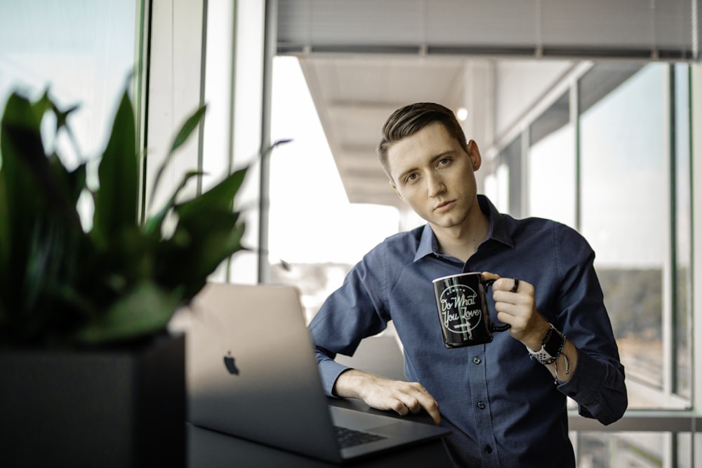 man in blue dress shirt holding black ceramic mug