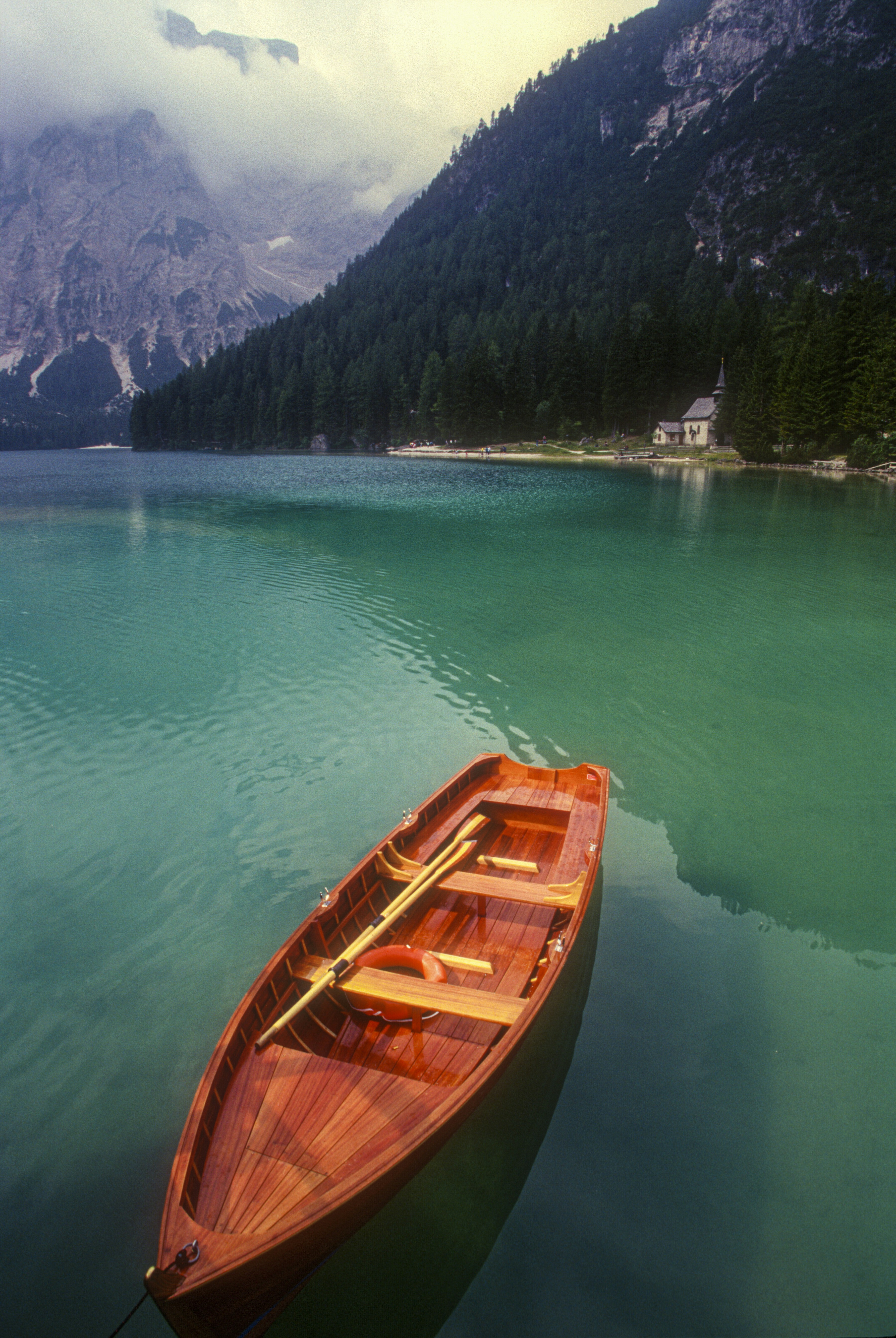 A solitary rental boat points out into the turquoise expanse of this beautiful lake in northern Italy. I shot it on slide film in 1999 and had to wait three weeks to see the image. Was so glad it came out beautifully.