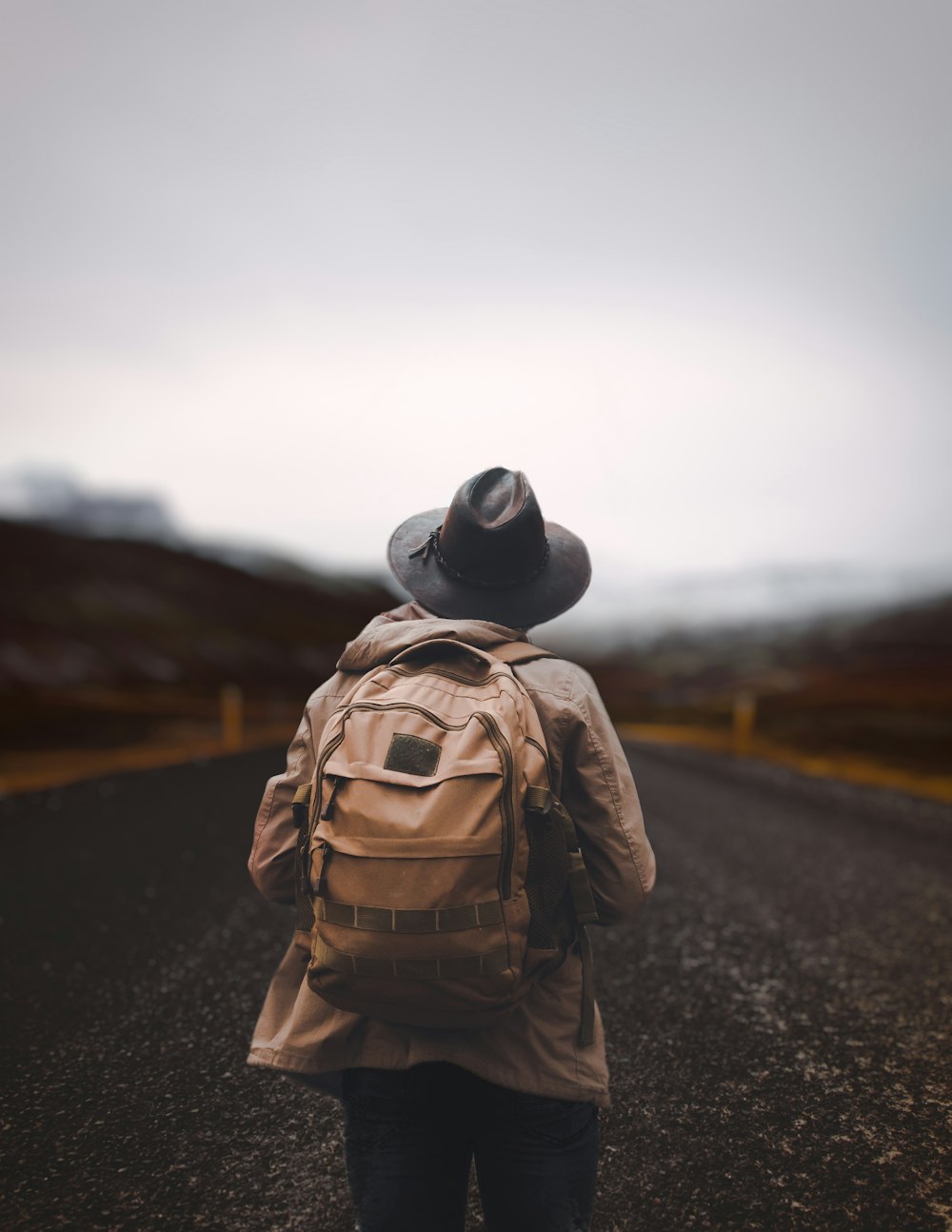 person in brown and black camouflage jacket and black hat walking on road during daytime