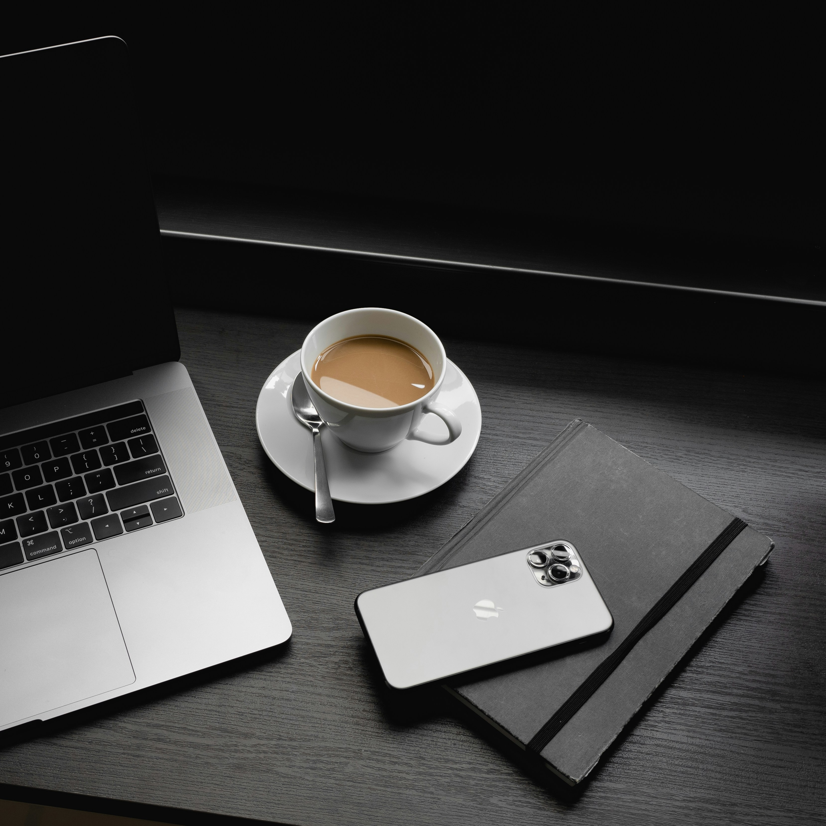 MacBook Proのそばに、ソーサーの上の白いセラミックのティーカップ