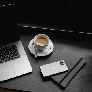 macbook pro beside white ceramic teacup on saucer