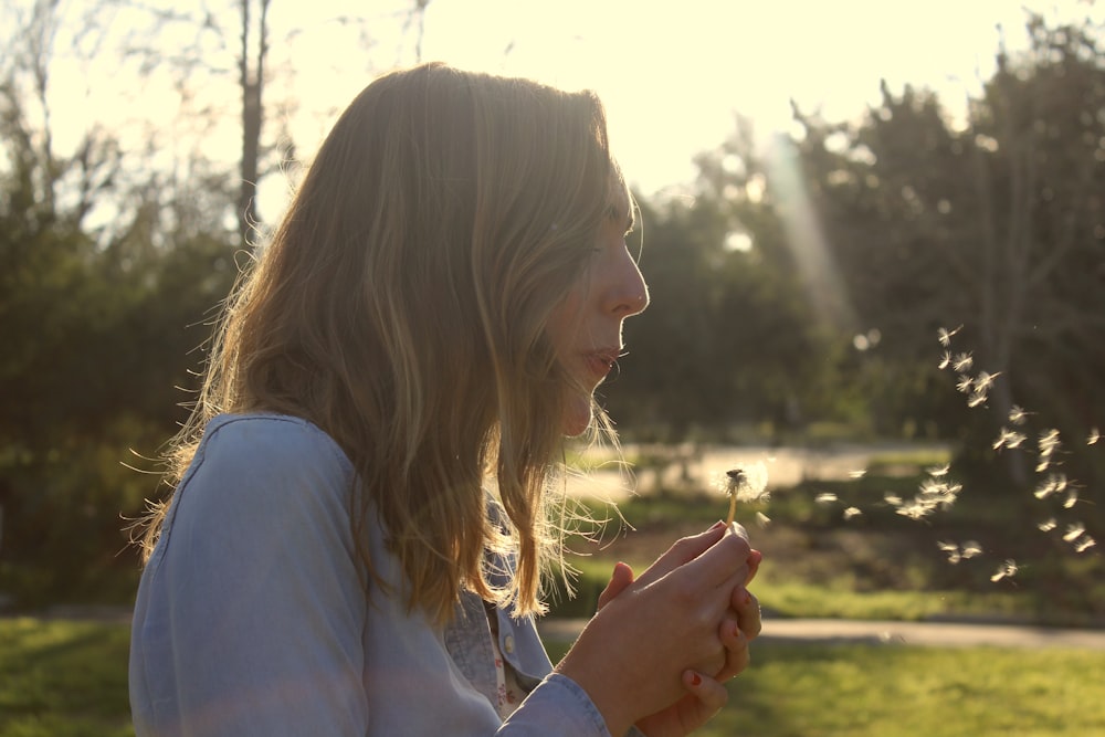 woman in blue shirt holding white dandelion flower during daytime