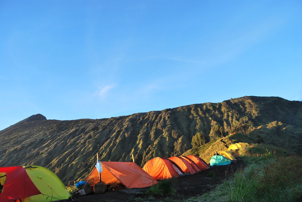 낮에는 푸른 하늘 아래 갈색 산 근처의 푸른 잔디밭에 있는 주황색과 회색 텐트