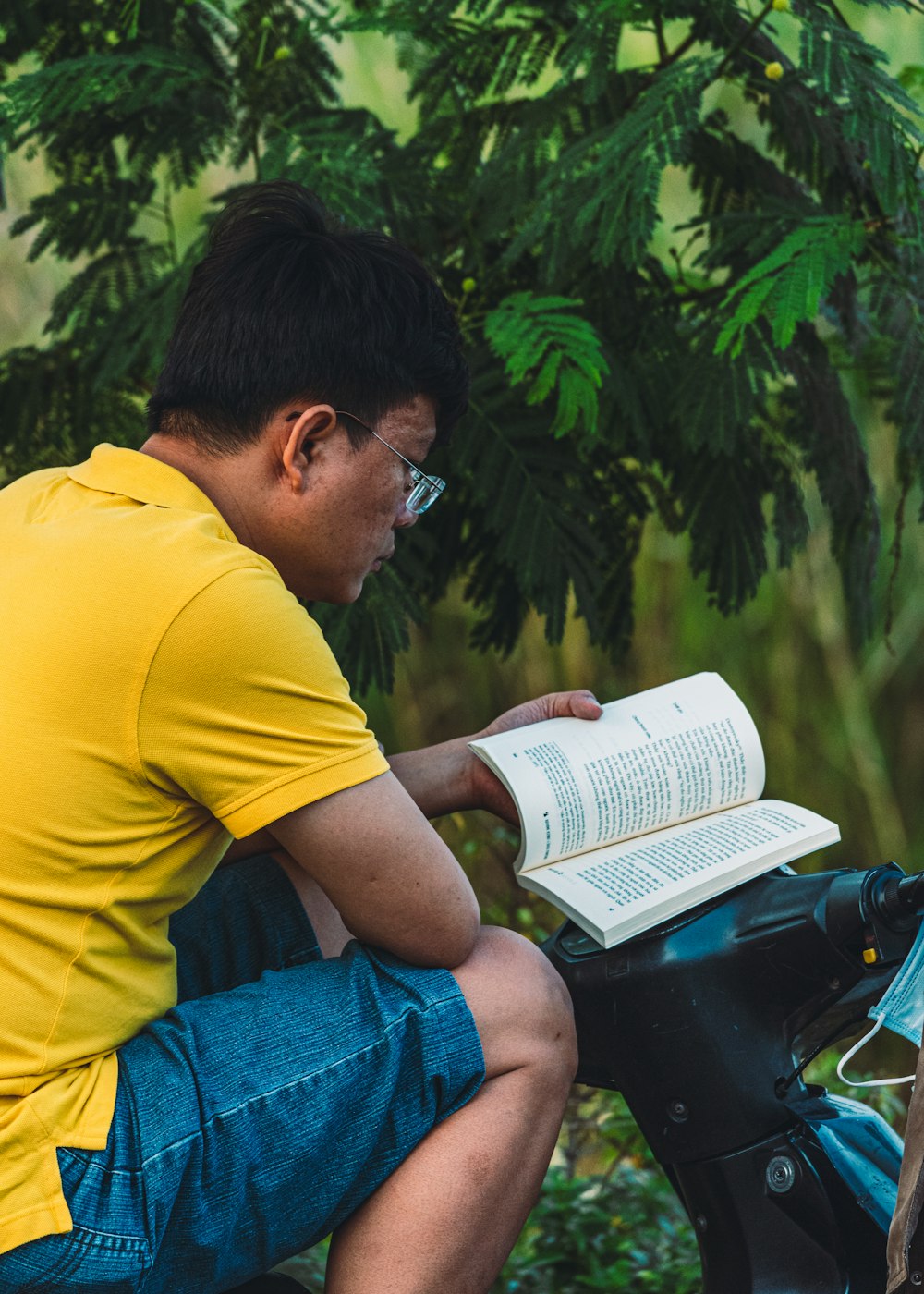 man in yellow t-shirt and blue denim jeans reading book