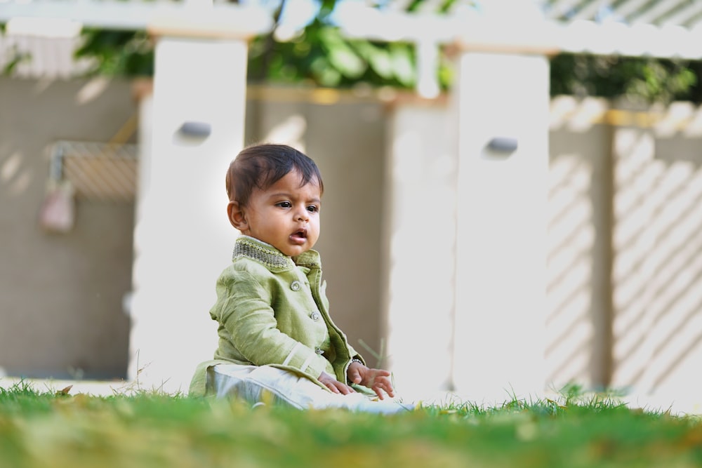 boy in green long sleeve shirt sitting on green grass during daytime