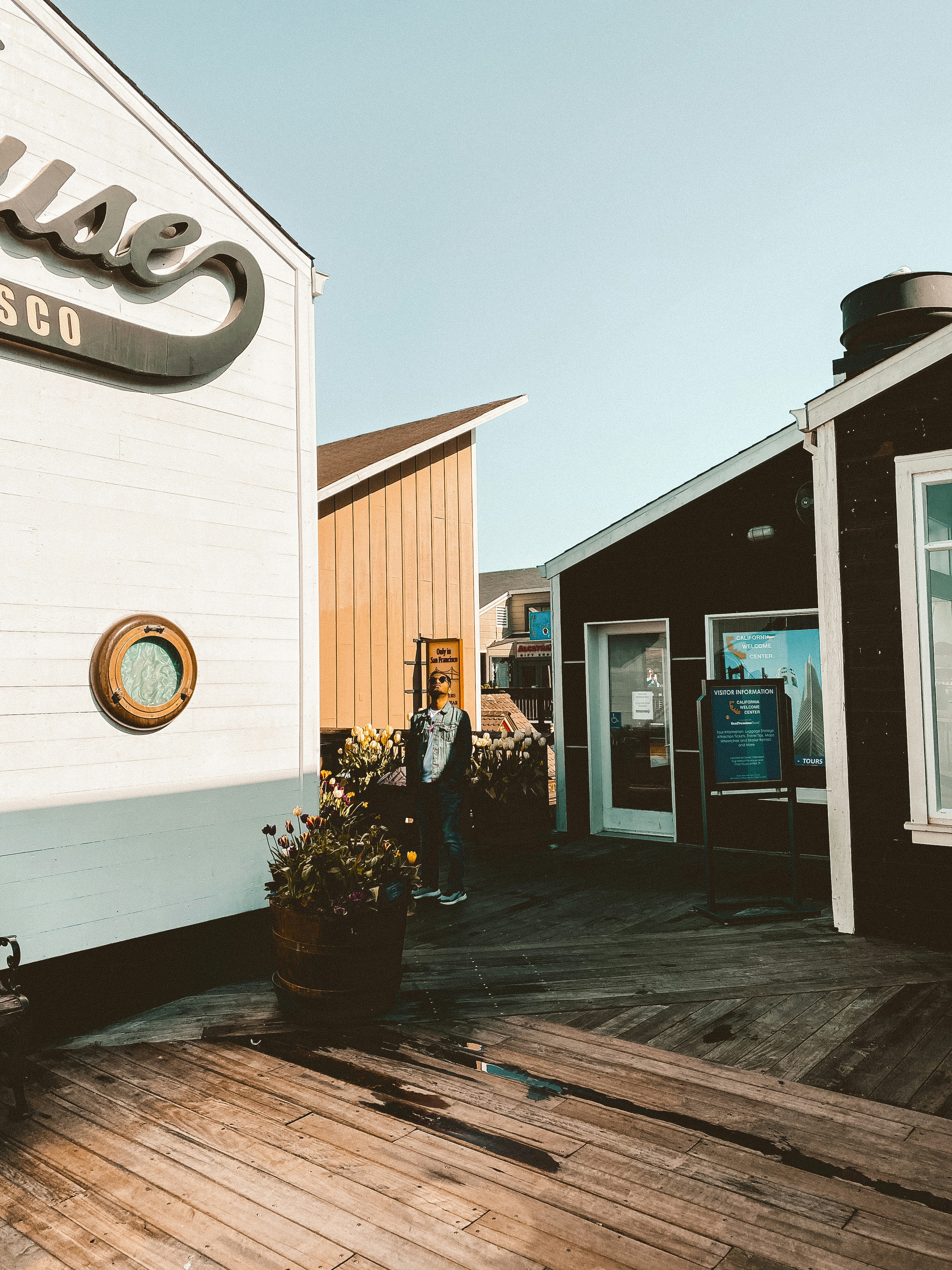 man in black jacket standing in front of white and blue store during daytime