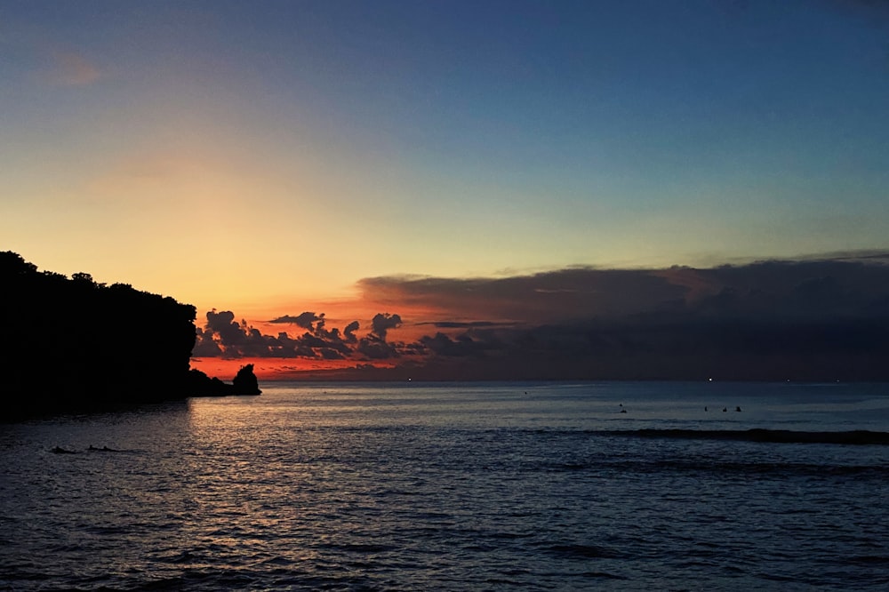 silhouette of rock formation on sea during sunset