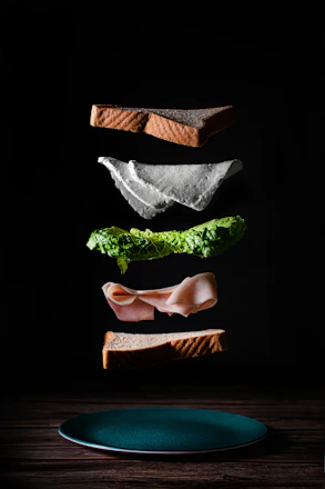 A chef demonstrating sandwich layering techniques to eager home cooks around a wooden table.