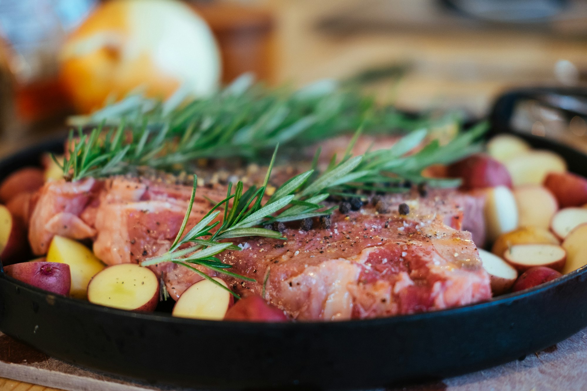 Steaks in a pan seasoned with sea salt, pepper, and rosemary with small potatoes spread around them to capture the au jus (that's french for tasty meat sauce).