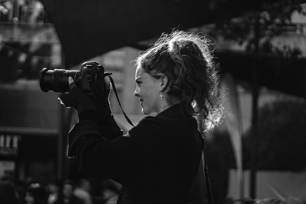 foto em tons de cinza da mulher na jaqueta preta segurando a câmera dslr