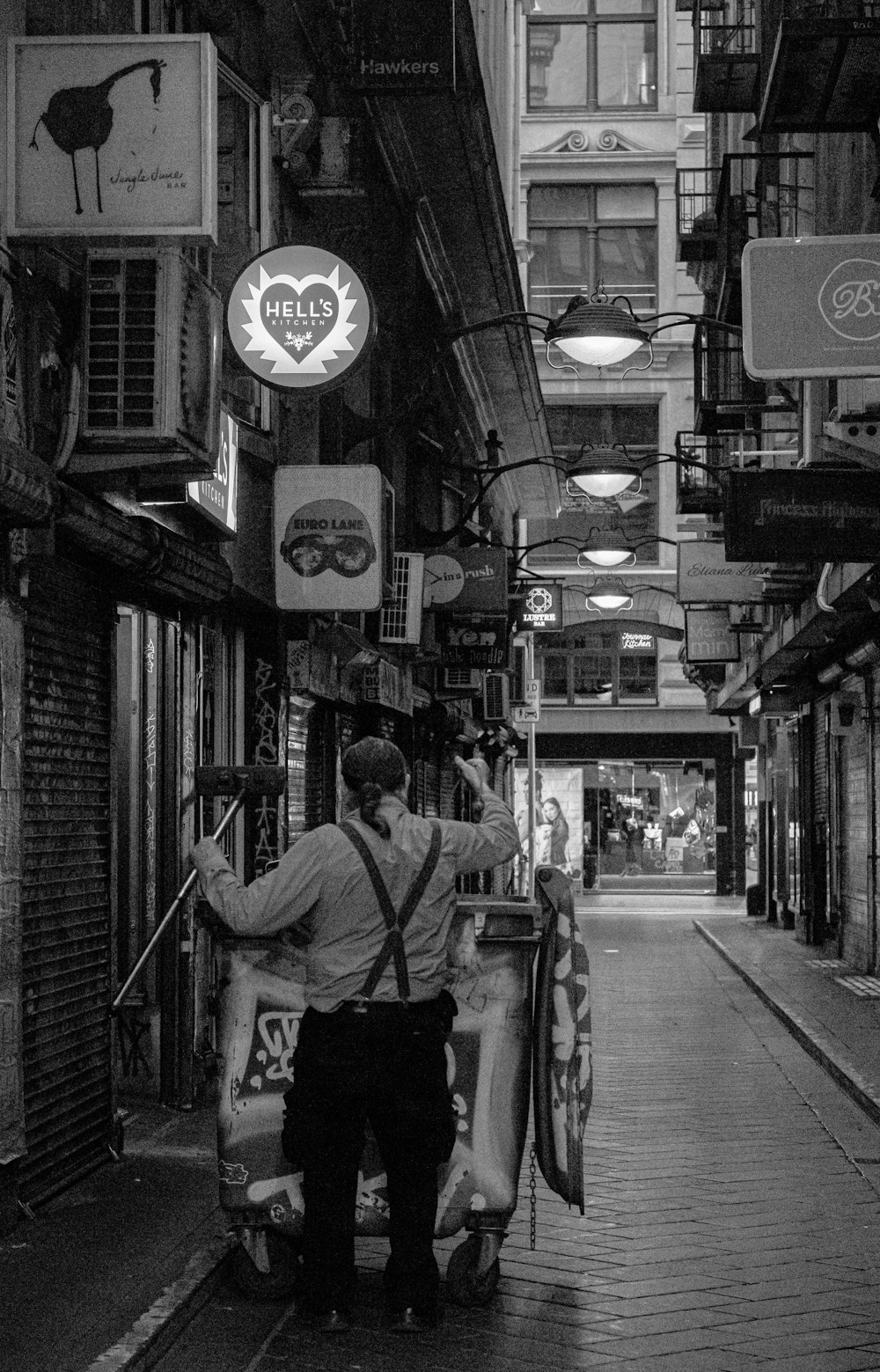 grayscale photo of man in white shirt and black pants standing on sidewalk