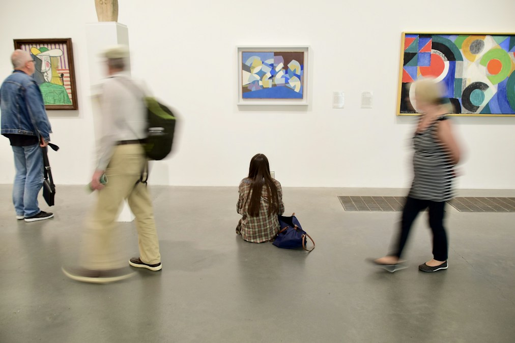 Visiteurs dans une salle de musée d’art moderne aux murs blancs, devant des toiles abstraites colorées