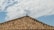 A rooftop covered with traditional terracotta tiles under a bright blue sky with scattered white clouds.