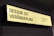 A rectangular, illuminated sign displays the phrase 'DESIGN IST VERÄNDERUNG' on the left side and 'DESIGN FOR CHANGE' on the right side. The sign has a yellow background with black text and is mounted against a tiled wall.
