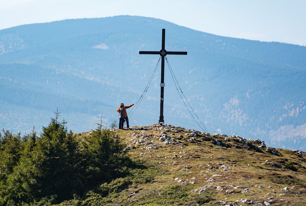 person standing on top of mountain near cross during daytime