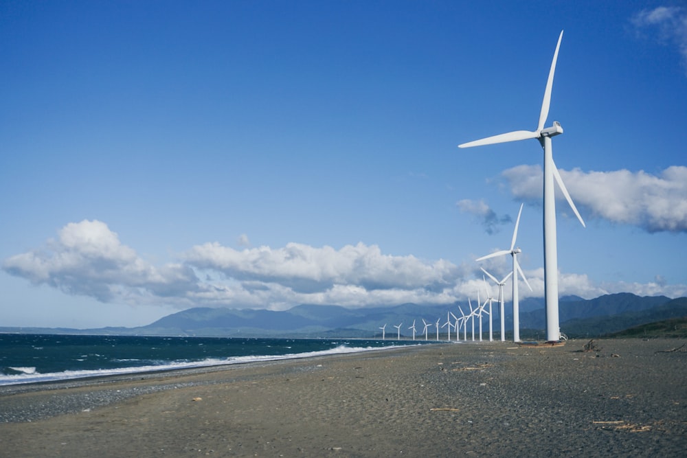 낮 동안 수역 근처의 회색 모래 위의 풍력 터빈