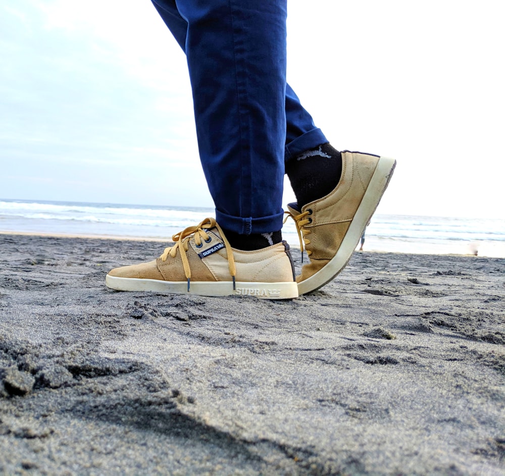 person in blue denim jeans and brown and white sneakers standing on beach during daytime
