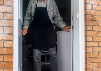 man in black vest and black dress pants standing beside white wooden door