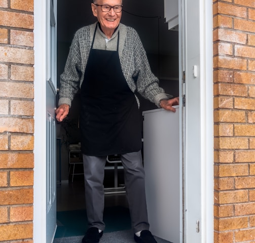 man in black vest and black dress pants standing beside white wooden door