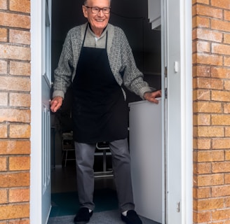 man in black vest and black dress pants standing beside white wooden door