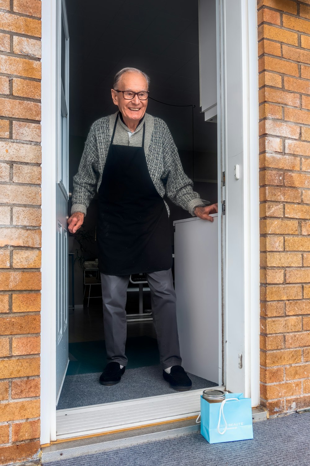 Hombre con chaleco negro y pantalones de vestir negros de pie junto a la puerta de madera blanca