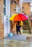 woman in brown jacket and blue denim jeans holding red umbrella
