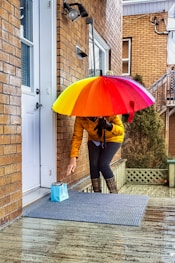 woman in brown jacket and blue denim jeans holding red umbrella