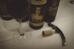 A vintage wine bottle and glass, with a glistening rich red wine catching light on an ivory linen table.