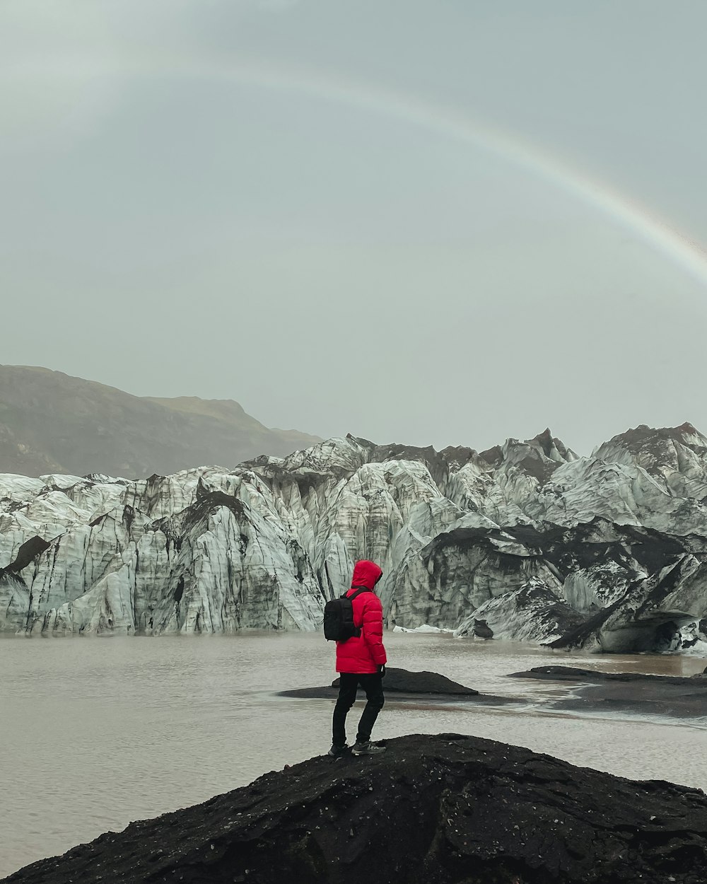 person in red jacket standing on brown sand near body of water during daytime