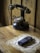 A vintage rotary telephone is placed on a wooden table next to an old mobile phone. The mobile phone rests on a crocheted doily, suggesting a blend of old and new technology. The background consists of wooden paneling, adding to the nostalgic aesthetic.