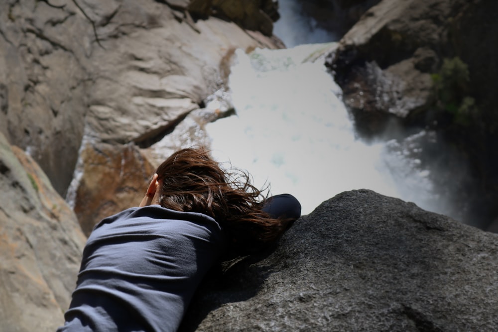 woman in black jacket sitting on rock near river during daytime