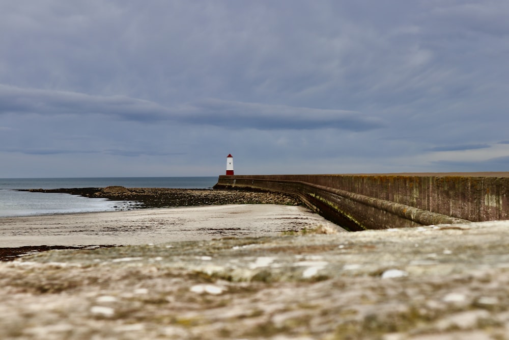 Phare blanc et rouge près d’un plan d’eau sous un ciel nuageux pendant la journée