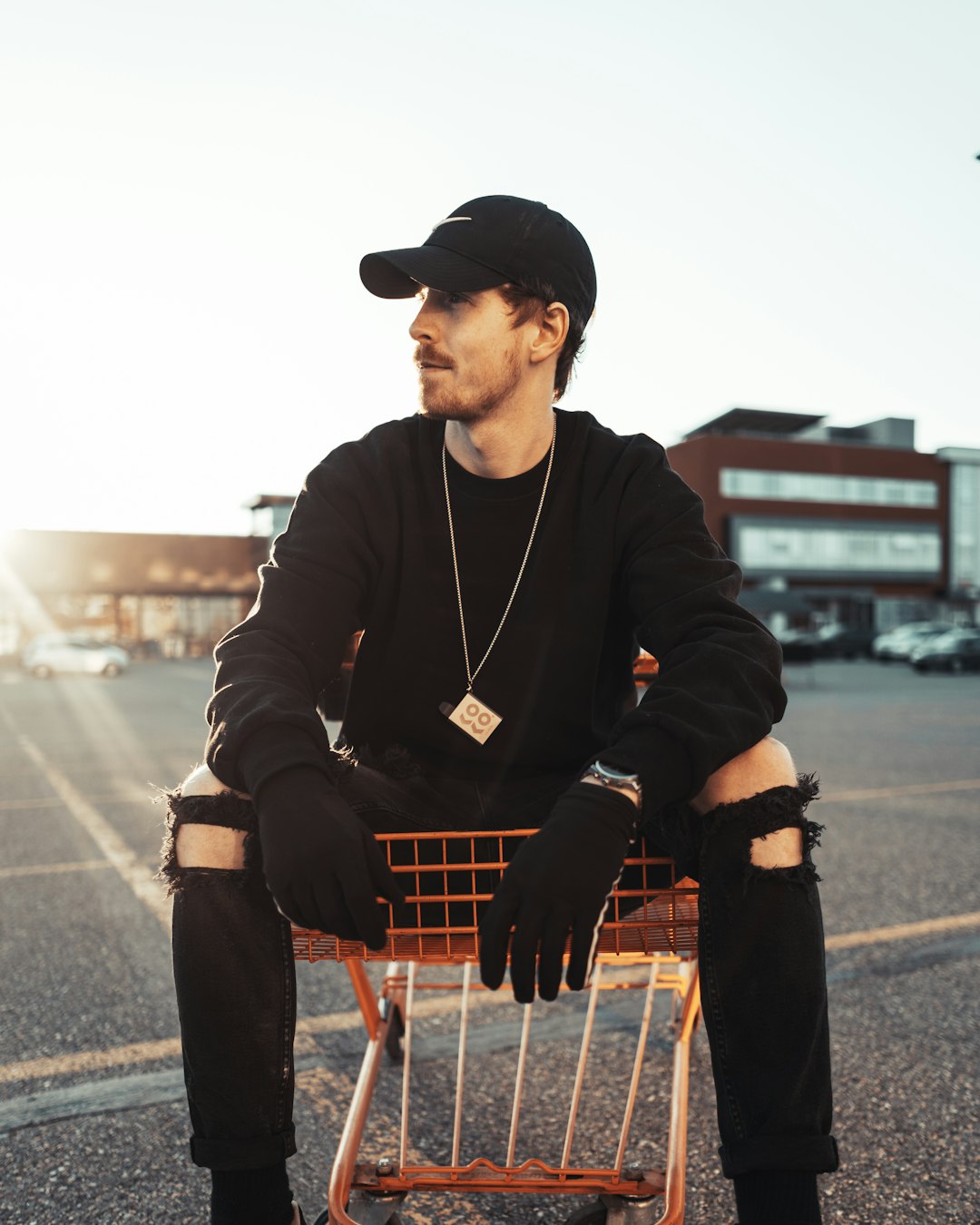 man in black jacket and black pants sitting on shopping cart