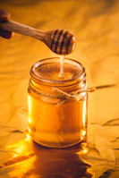 Hands extracting golden honey dripping from a fresh honeycomb into a jar