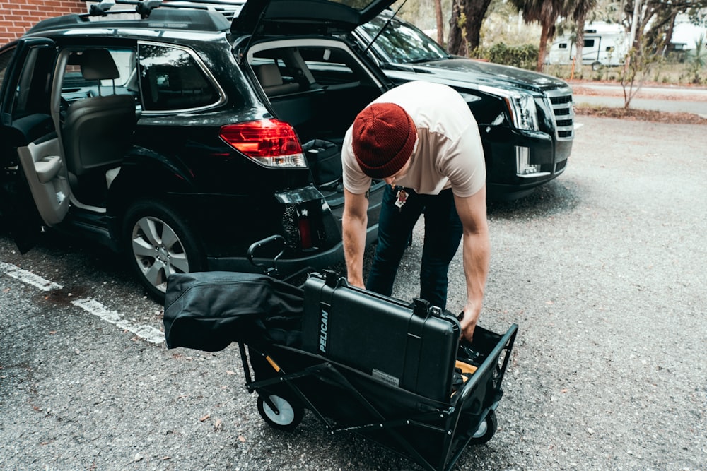 man in gray t-shirt and black shorts holding black stroller near black suv during daytime