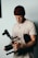 A person wearing a brown beanie and a light beige shirt is holding a professional camera rig. The camera appears to be equipped with additional gear, suggesting a focus on filmmaking or video production.