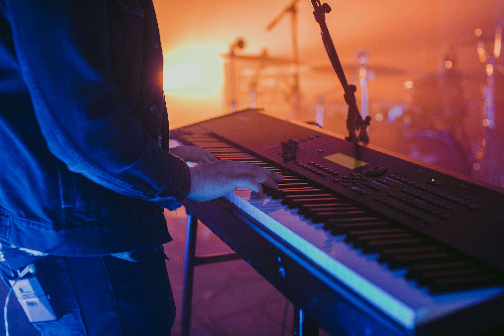 Keyboard vs. piano: person's hands playing a digital piano on stage.