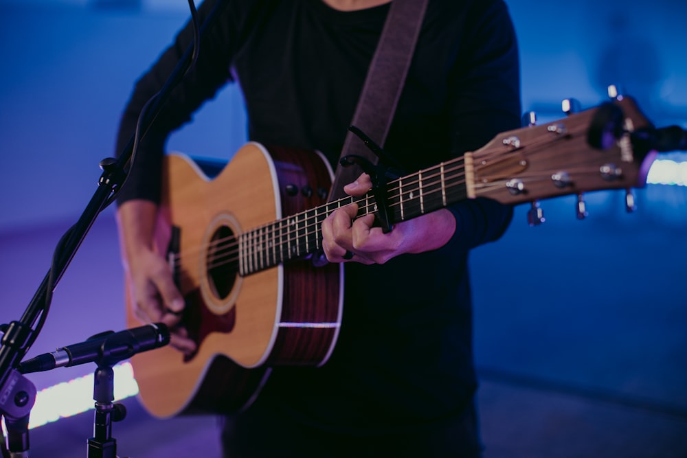 uomo in camicia nera a maniche lunghe che suona la chitarra acustica marrone