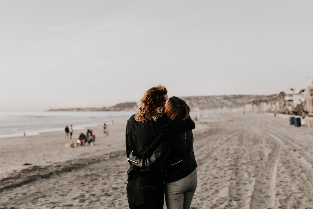 woman in black jacket and gray pants walking on beach during daytime