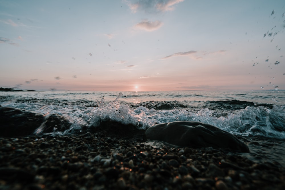 the sun is setting over the ocean with rocks in the foreground