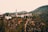 A small village is nestled in a mountainous landscape. The village features a prominent mosque with a tall minaret, surrounded by houses scattered across the hillside. The vegetation appears lush, and the hills in the background create a picturesque setting.