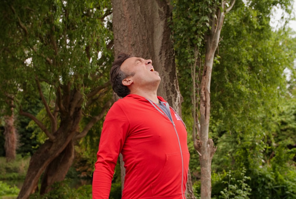 man in red long sleeve shirt standing beside brown tree during daytime