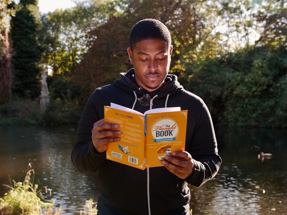 man in black and white hoodie holding yellow book