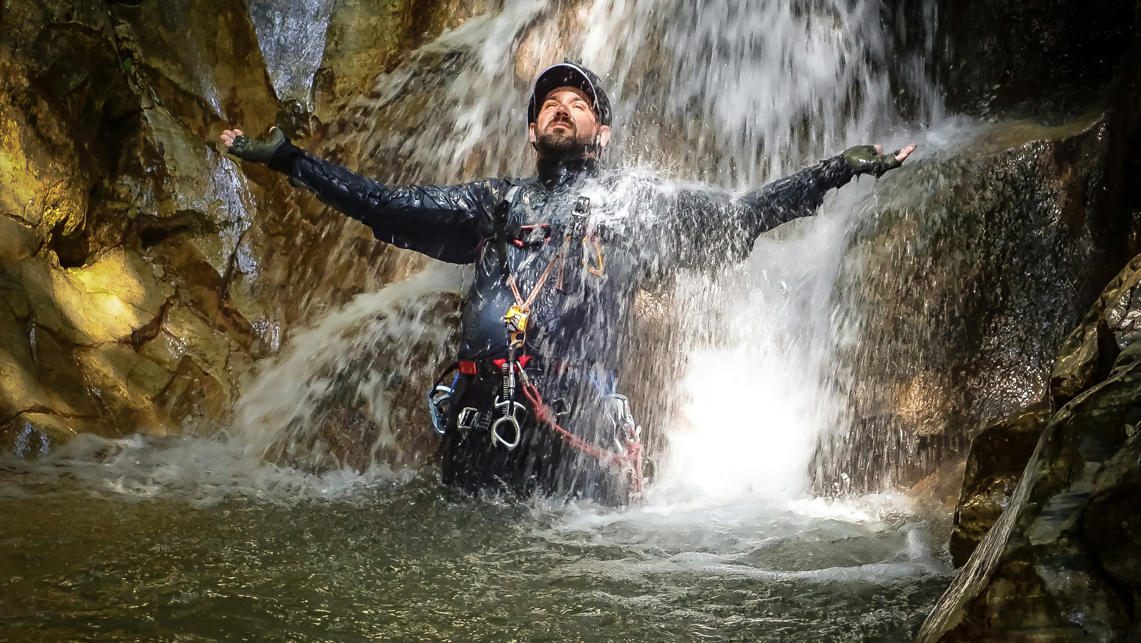 Caver emerging through a narrow cave passage, headlamp illuminating stalactite formations