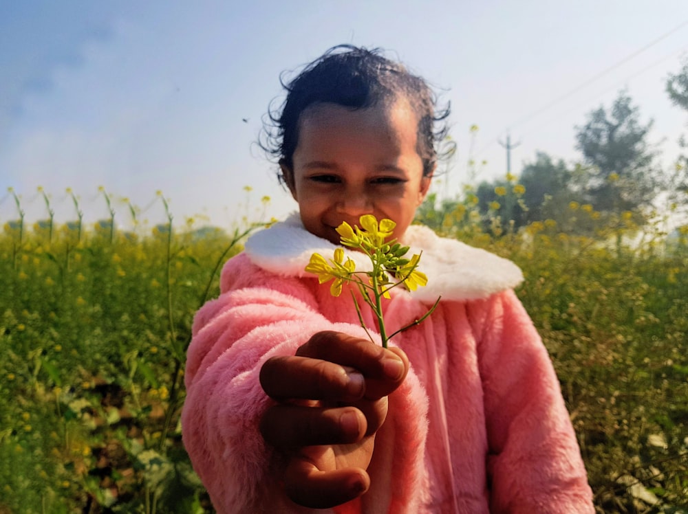 girl in pink jacket holding yellow flower