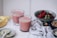 Two glasses of pink smoothie with sprinkled seeds on top are placed on a marble surface. A peeled banana lies nearby alongside a plate with a spoon containing seeds. A bowl filled with fresh strawberries and another small bowl with nuts are present in the background. A soft, white cloth is draped casually around the items.