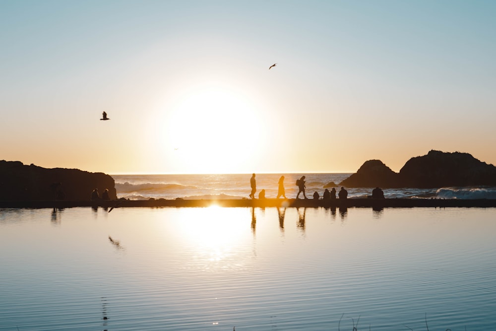 silhueta das pessoas na praia durante o pôr do sol
