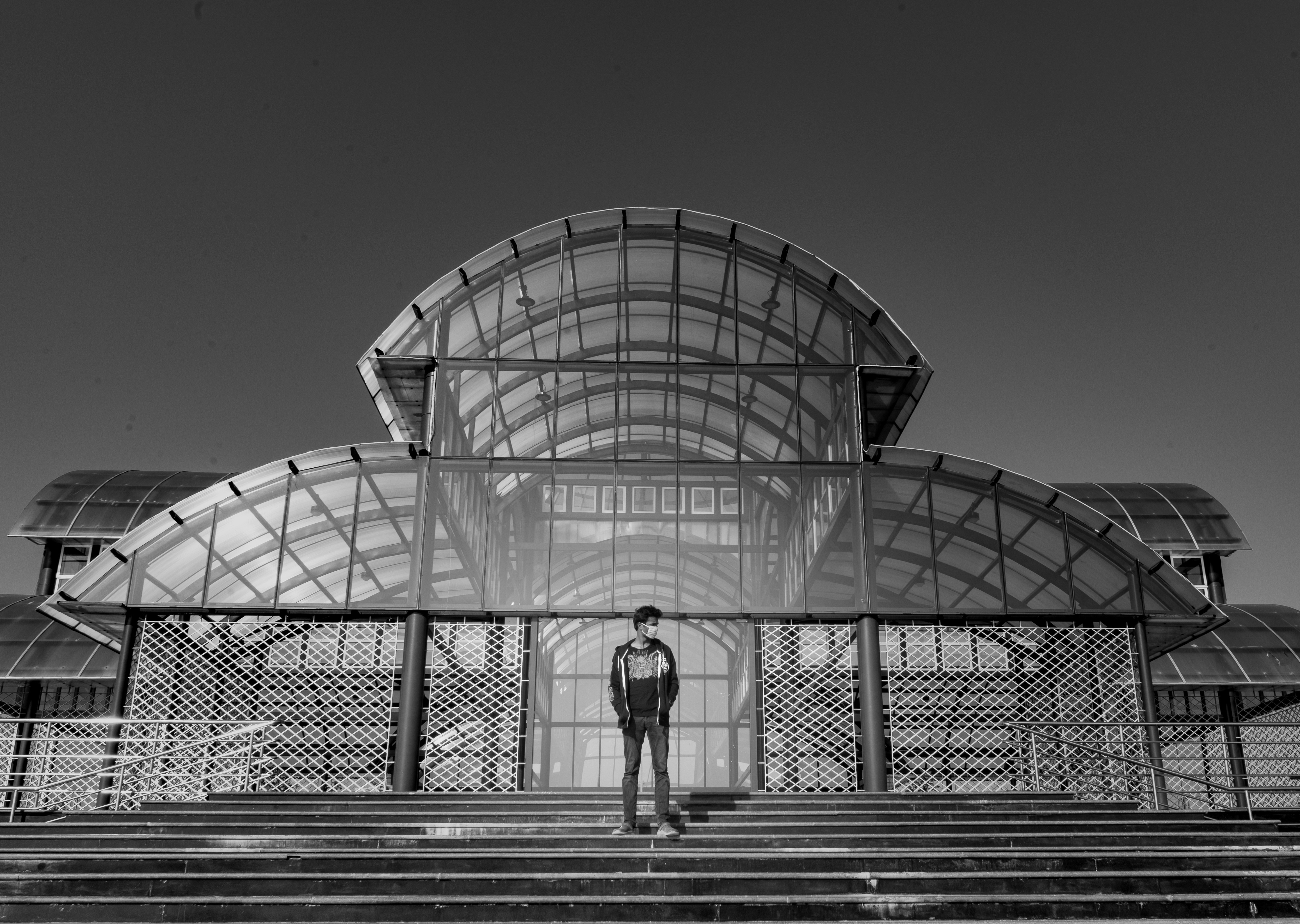 grayscale photo of woman in black shirt and pants standing near glass building