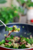 Close-up of a sturdy metal scoop and a frying pan with fresh vegetables inside.